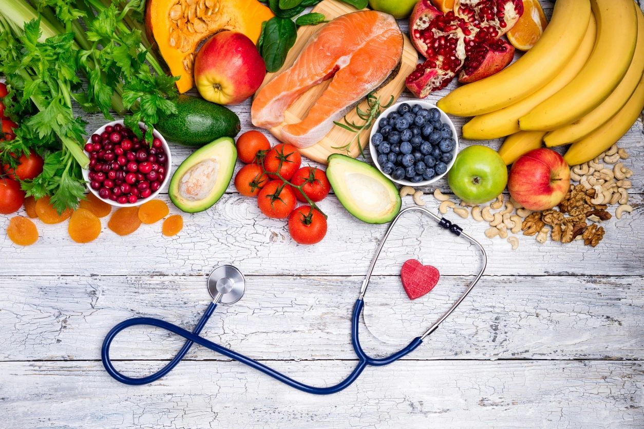 A variety of fresh fruits, vegetables, and salmon arranged with a stethoscope, symbolizing health and nutrition.